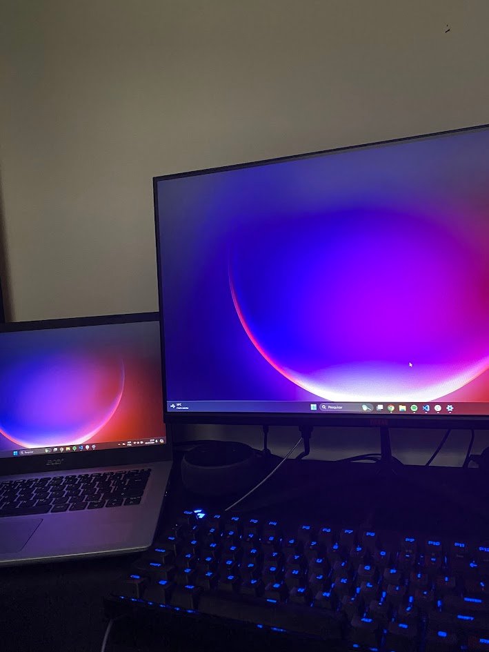 Mesa à noite com um notebook ao lado de um monitor e um teclado com luz azul