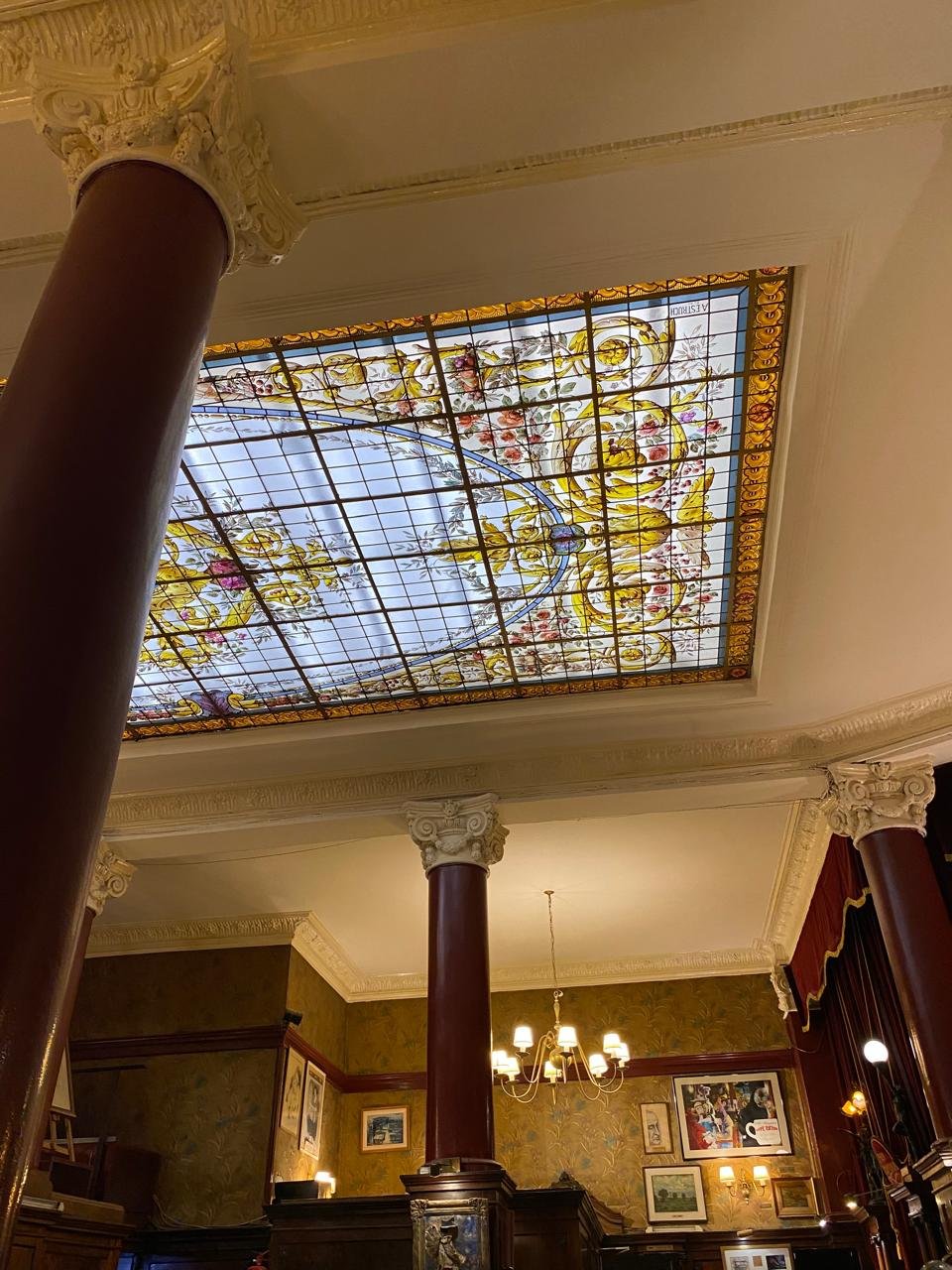 Teto de vitral ornamentado sustentado por colunas vermelho-escuras num café antigo de Buenos Aires