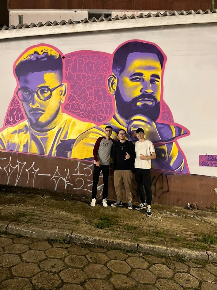 Três amigos posando em frente a um mural colorido à noite