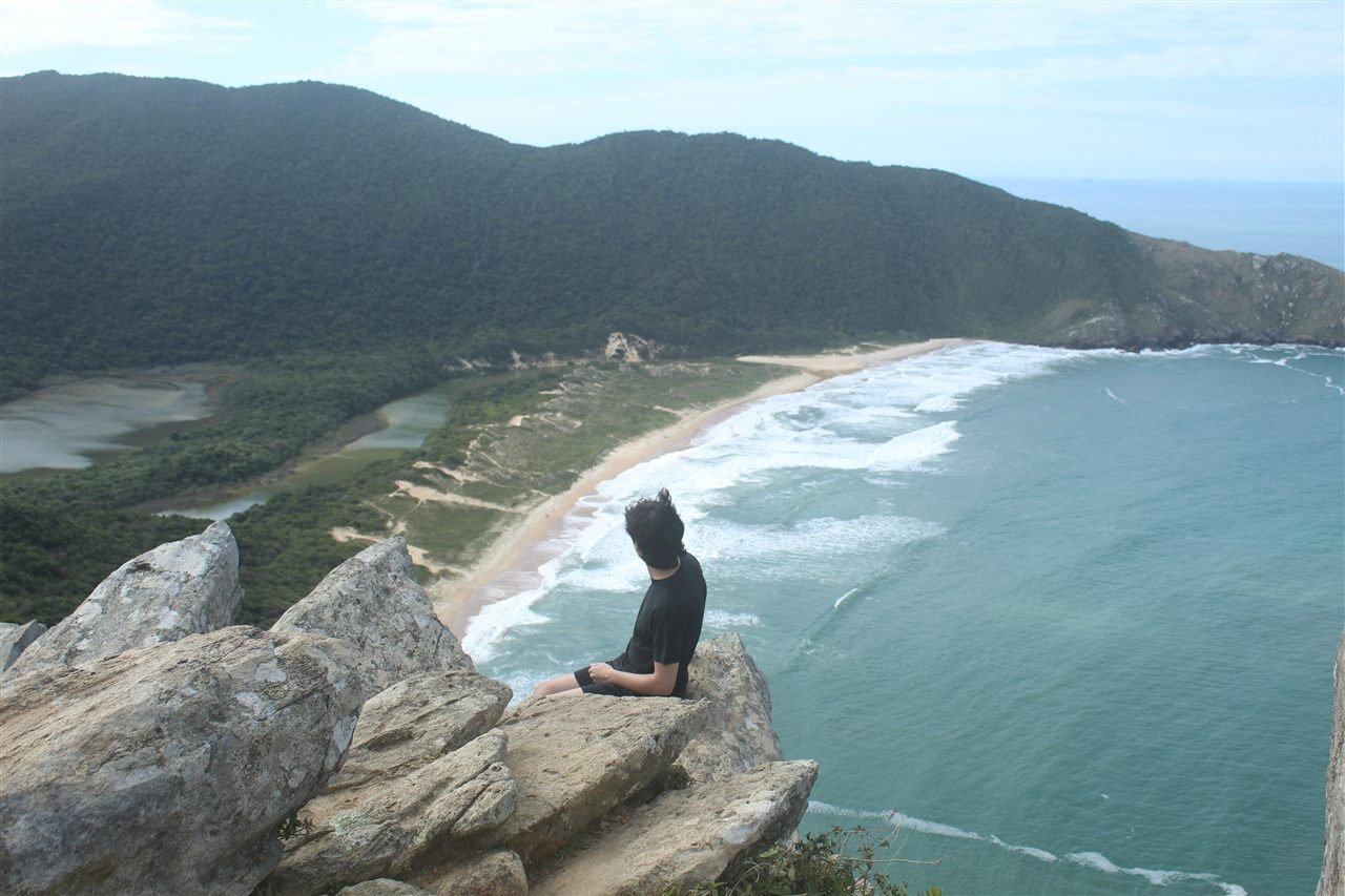 Sentado nas pedras no alto de um morro, olhando lá pra baixo para a praia, a lagoa e os morros verdes